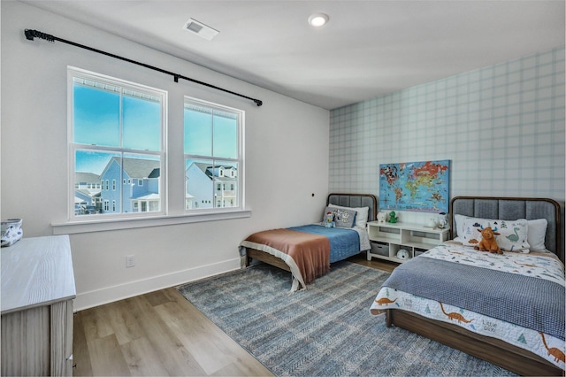 bedroom with wood finished floors, visible vents, baseboards, wallpapered walls, and an accent wall