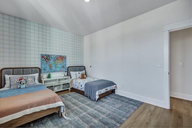 bedroom with wallpapered walls, an accent wall, baseboards, and wood finished floors