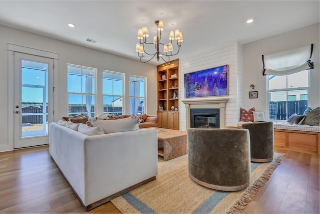 living area with a glass covered fireplace, built in features, plenty of natural light, and wood-type flooring