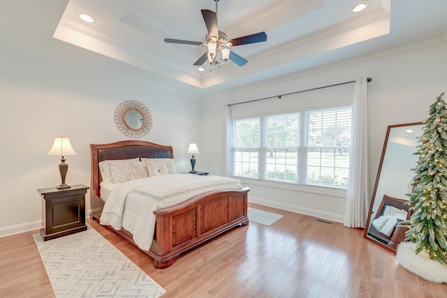 bedroom with light wood finished floors, baseboards, visible vents, and a tray ceiling