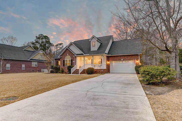 view of front of house with driveway, an attached garage, covered porch, a front lawn, and brick siding