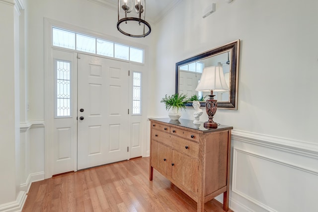 entrance foyer with light wood-type flooring, a wainscoted wall, and crown molding