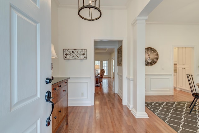 entrance foyer featuring crown molding, light wood-type flooring, wainscoting, and decorative columns