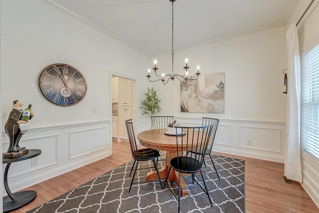 dining space with a wainscoted wall, light wood-style flooring, crown molding, and a notable chandelier