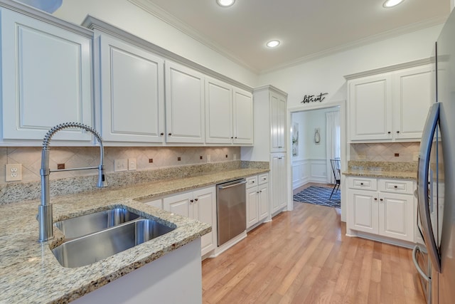 kitchen with ornamental molding, stainless steel appliances, light wood-type flooring, white cabinetry, and a sink