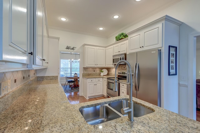 kitchen featuring backsplash, appliances with stainless steel finishes, ornamental molding, white cabinets, and light stone countertops