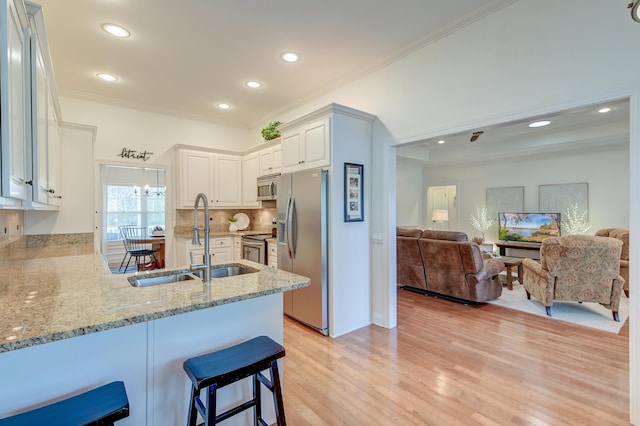 kitchen featuring light stone counters, a peninsula, stainless steel appliances, crown molding, and a sink