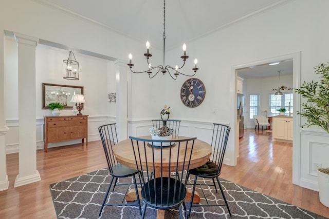 dining space with a chandelier, a decorative wall, ornate columns, light wood finished floors, and crown molding