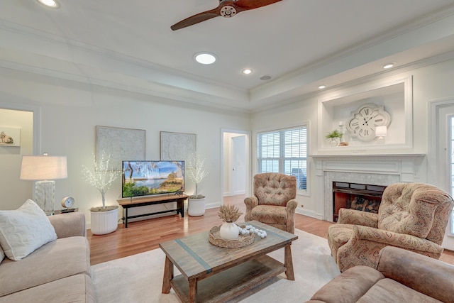 living room featuring a raised ceiling, a premium fireplace, crown molding, light wood-style floors, and recessed lighting