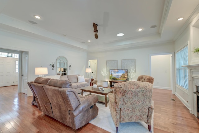 living area with light wood-style flooring, recessed lighting, a fireplace, a raised ceiling, and crown molding