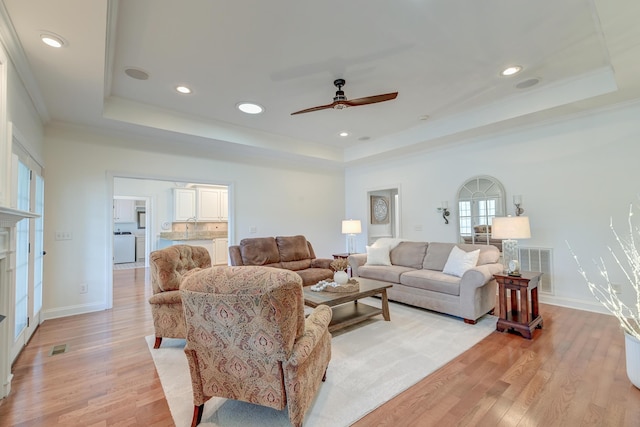 living area with a tray ceiling, baseboards, crown molding, and light wood finished floors