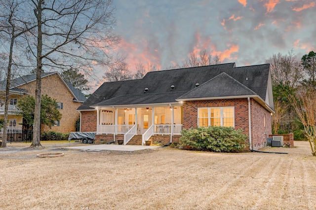 view of front facade featuring roof with shingles, crawl space, covered porch, cooling unit, and brick siding