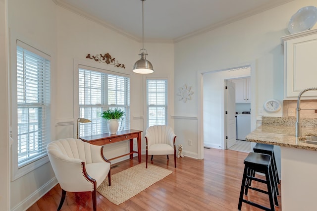 living area with washer / dryer, plenty of natural light, ornamental molding, and light wood-style floors