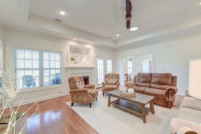 living area featuring baseboards, a tray ceiling, light wood-type flooring, and crown molding