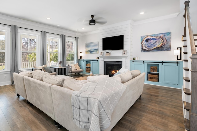 living area featuring a glass covered fireplace, stairway, dark wood finished floors, and a ceiling fan