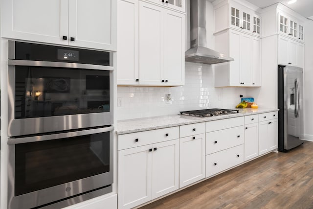 kitchen featuring stainless steel appliances, white cabinets, wall chimney range hood, decorative backsplash, and dark wood-style flooring