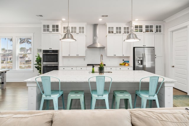 kitchen with a center island with sink, tasteful backsplash, stainless steel appliances, crown molding, and wall chimney range hood