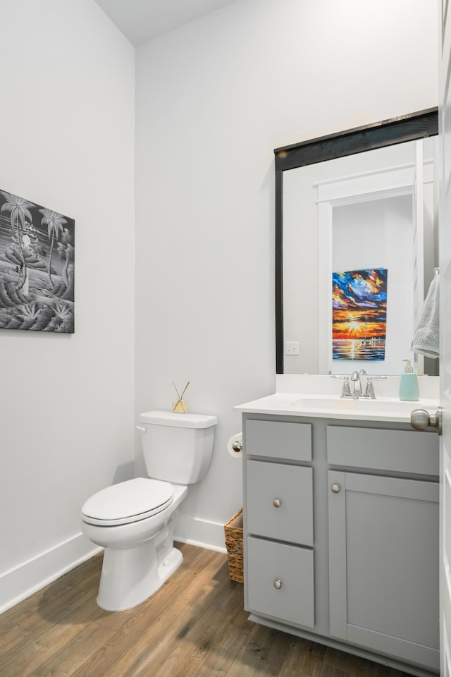 half bathroom with toilet, vanity, baseboards, and wood finished floors