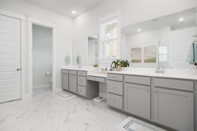 bathroom with baseboards, toilet, two vanities, marble finish floor, and a sink