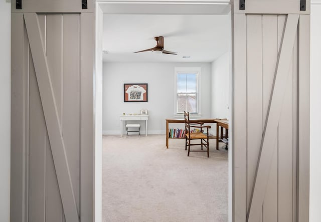 office space with visible vents, a barn door, carpet floors, baseboards, and ceiling fan