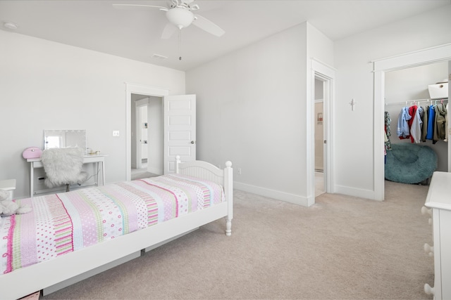 bedroom with light carpet, a ceiling fan, a closet, baseboards, and a spacious closet