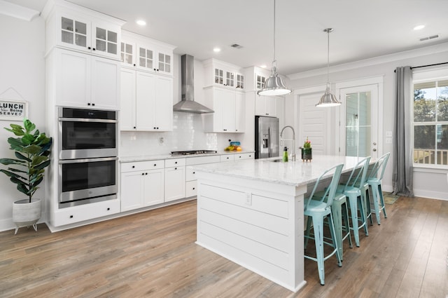 kitchen featuring visible vents, backsplash, wall chimney range hood, stainless steel appliances, and a kitchen island with sink