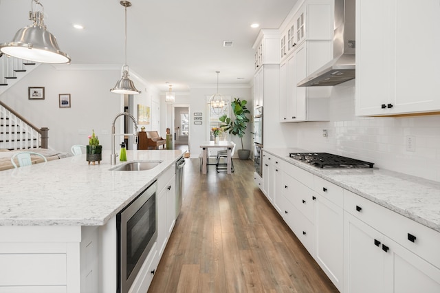 kitchen with ornamental molding, a sink, backsplash, appliances with stainless steel finishes, and wall chimney range hood