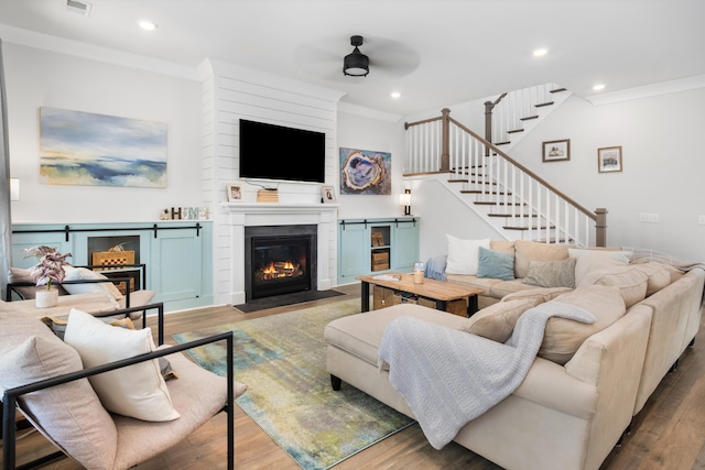 living area featuring wood finished floors, recessed lighting, ceiling fan, crown molding, and a large fireplace