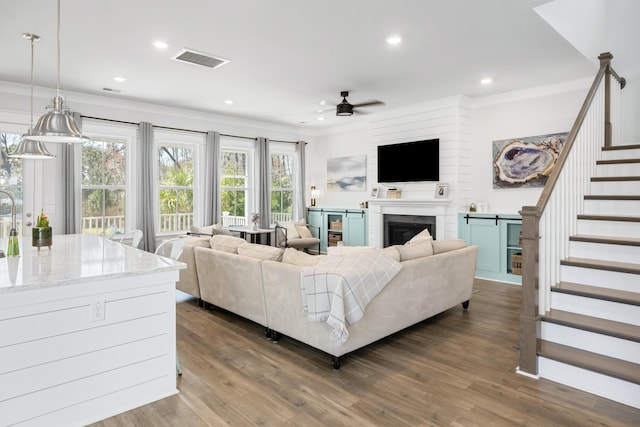 living area with visible vents, stairway, crown molding, ceiling fan, and dark wood-style flooring