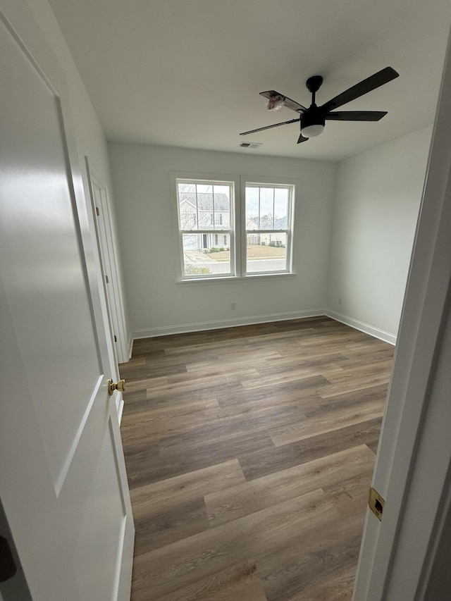 spare room featuring visible vents, ceiling fan, baseboards, and wood finished floors