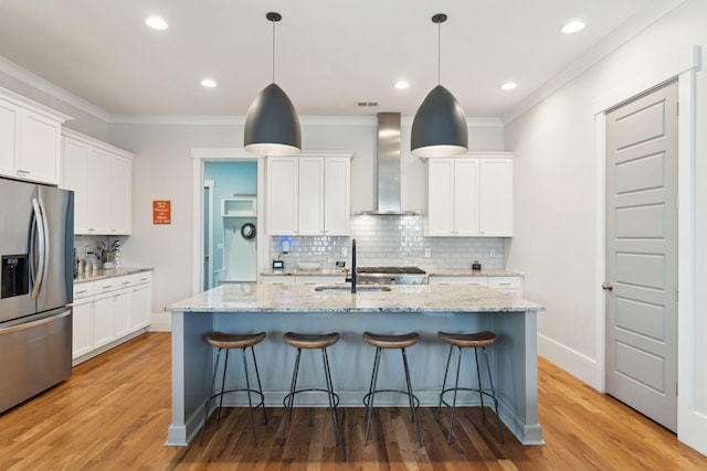 kitchen with an island with sink, white cabinetry, wall chimney exhaust hood, and stainless steel fridge