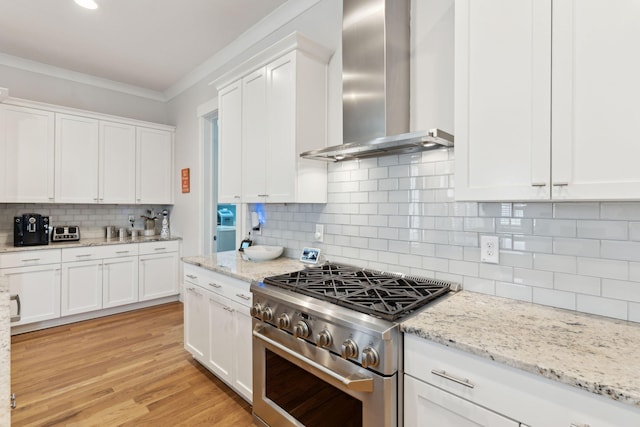 kitchen with decorative backsplash, white cabinets, high end range, and wall chimney exhaust hood