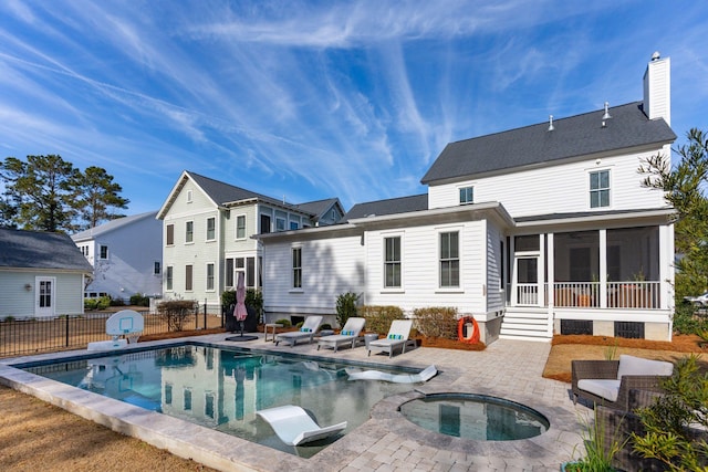 rear view of property featuring a patio area, a pool with hot tub, and a sunroom