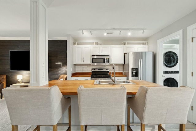 kitchen with decorative backsplash, white cabinets, stacked washer and clothes dryer, appliances with stainless steel finishes, and wooden counters