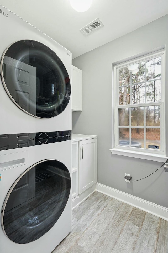 laundry room featuring cabinet space, visible vents, light wood-style floors, and stacked washer and clothes dryer