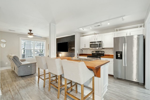 kitchen with butcher block countertops, appliances with stainless steel finishes, a breakfast bar area, white cabinetry, and a sink