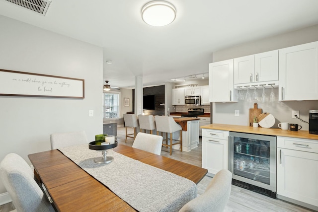 dining room with light wood finished floors, wine cooler, a dry bar, and visible vents