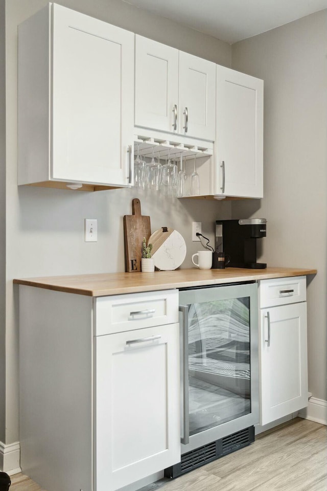 bar featuring wine cooler, baseboards, light wood-style flooring, and a dry bar