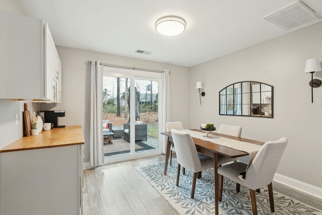 dining space with light wood-type flooring, visible vents, and baseboards