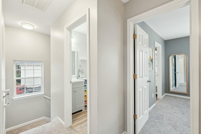 corridor with baseboards, visible vents, and light colored carpet