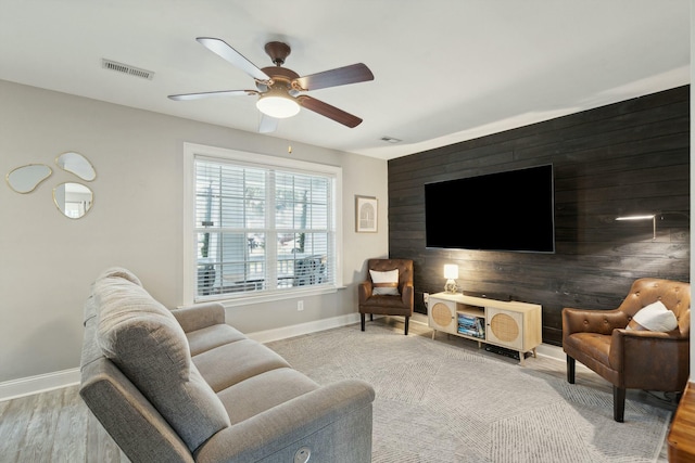 living room featuring baseboards, an accent wall, visible vents, and a ceiling fan