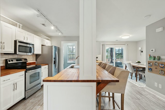 kitchen with white cabinets, appliances with stainless steel finishes, wooden counters, and a breakfast bar area