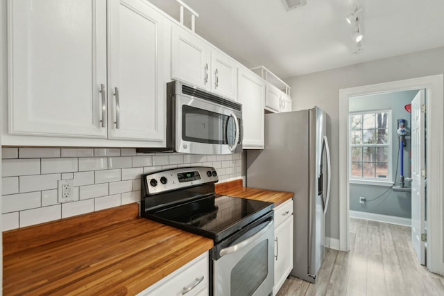 kitchen with light wood finished floors, butcher block counters, appliances with stainless steel finishes, white cabinetry, and backsplash