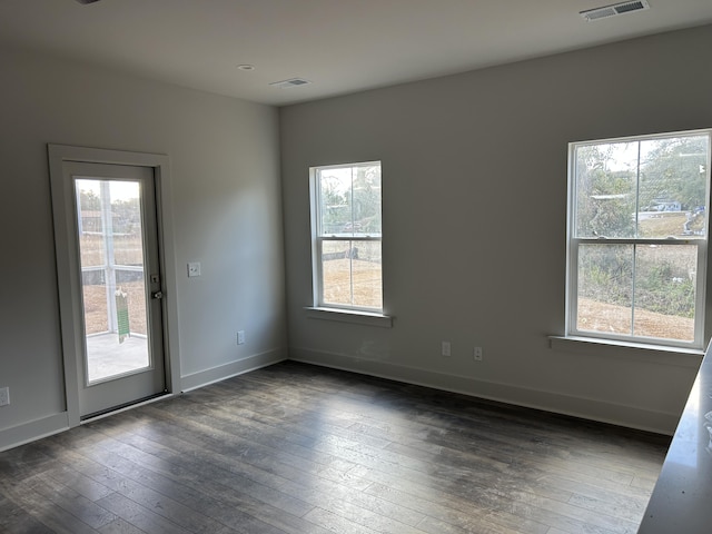 spare room with dark wood-type flooring, visible vents, and baseboards