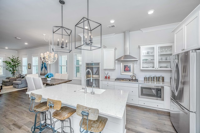 kitchen featuring white cabinets, an island with sink, wall chimney exhaust hood, and appliances with stainless steel finishes