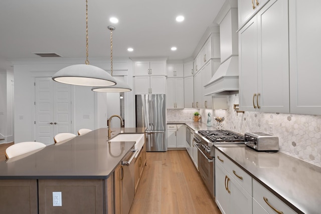 3226 Waverly Ln, Johns Island, SC 29455 - kitchen with appliances with stainless steel finishes, custom range hood, light wood-type flooring, a center island with sink, and backsplash