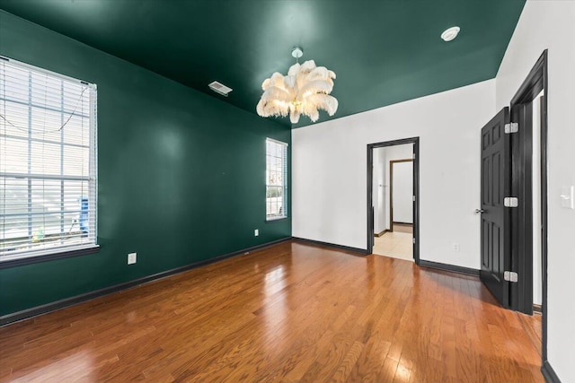 unfurnished room with a notable chandelier, wood finished floors, visible vents, and baseboards