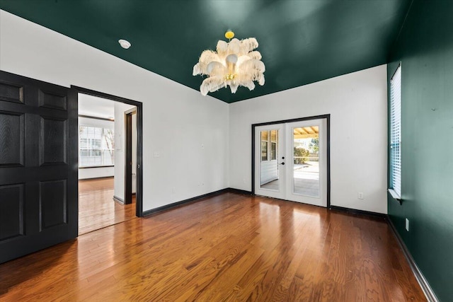 unfurnished room with a chandelier, baseboards, and wood finished floors