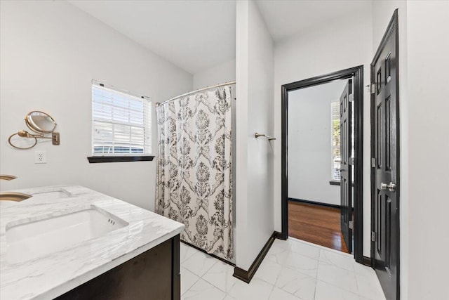 bathroom featuring a shower with curtain, baseboards, double vanity, a sink, and marble finish floor