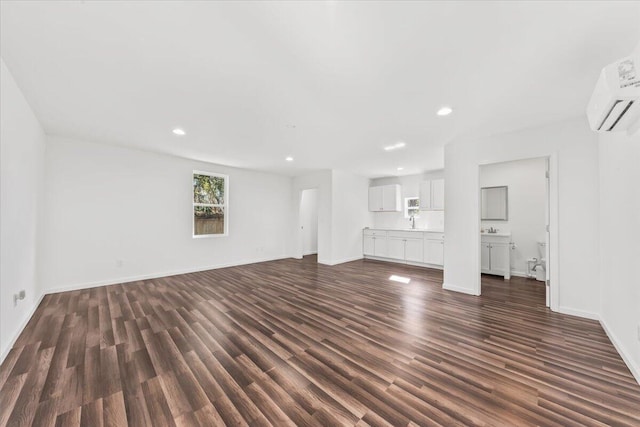 unfurnished living room featuring a wall mounted air conditioner, a sink, dark wood-style floors, recessed lighting, and baseboards